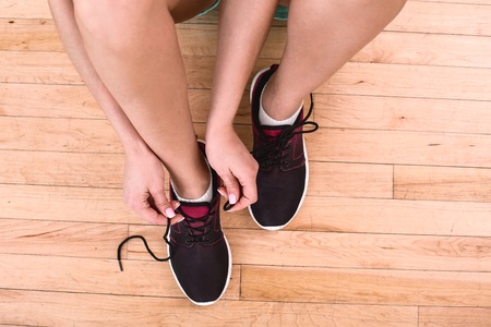 Top view photo of young sporty woman. Fitness girl sitting on floor and tying shoelaces. Focus on sneakersの写真素材
