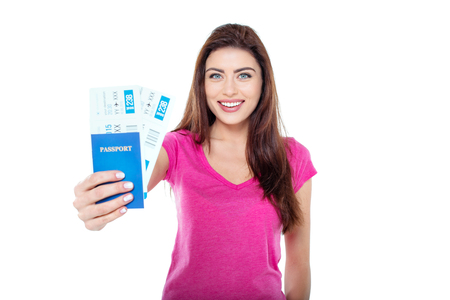 Studio shot of beautiful young brunette woman. Pretty girl holding tickets and passport, cheerfully smiling and looking at camera. Isolated backgroundの写真素材
