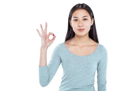 Studio shot of beautiful young asian woman. Pretty girl looking at camera and showing ok sign. Isolated backgroundの写真素材