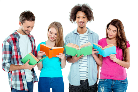 Studio shot of nice young multicultural friends. Beautiful people reading books. One boy looking at camera and smiling. Isolated backgroundの写真素材