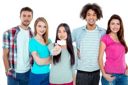 Studio shot of nice young multicultural friends. Beautiful people looking at camera and smiling. One girl in the middle holding empty visit card. Isolated backgroundの写真素材