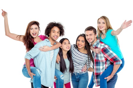 Studio shot of nice young multicultural friends. Beautiful people looking at camera and smiling. Two guys carrying girls piggyback. Isolated backgroundの写真素材