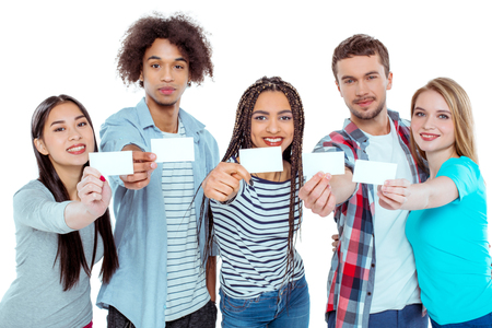 Studio shot of nice young multicultural friends. Beautiful people looking at camera, smiling and holding empty visit cards. Isolated backgroundの写真素材