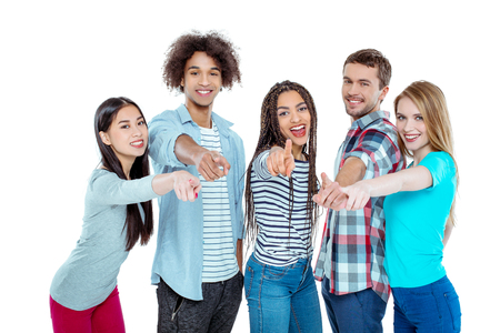 Studio shot of nice young multicultural friends. Beautiful people looking at camera, smiling and pointing at camera. Isolated backgroundの写真素材