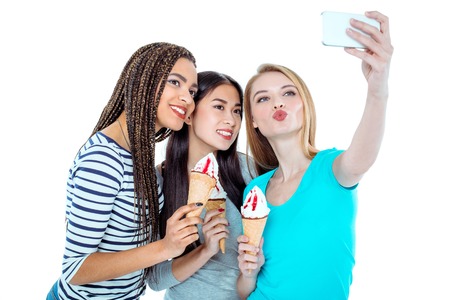 Studio shot of nice young friends. Beautiful girls holding ice-creams, making selfie photo on mobile...