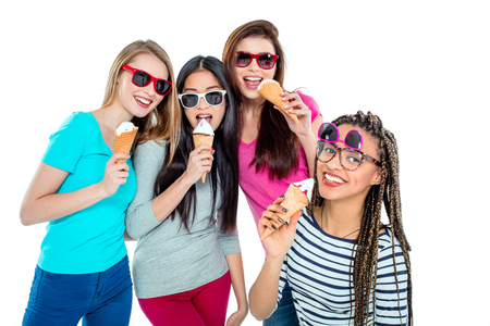 Studio shot of nice young friends. Beautiful girls looking at camera, holding ice-creams, wearing sunglasses and smiling. Isolated backgroundの写真素材