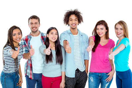 Studio shot of nice young multicultural friends. Beautiful people showing thumbs up, looking at camera and cheerfully smiling. Isolated backgroundの写真素材