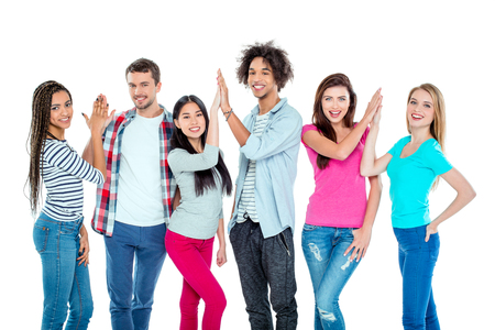 Studio shot of nice young multicultural friends. Beautiful people making high fives, looking at camera and cheerfully smiling. Isolated backgroundの写真素材