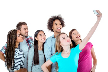 Studio shot of nice young multicultural friends. Beautiful people smiling and making selfie photo on mobile phone. Isolated backgroundの写真素材