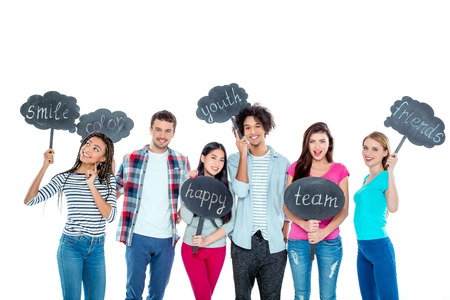 Studio shot of nice young multicultural friends. Beautiful people looking at camera, holding nameplates with different words and smiling. Isolated backgroundの写真素材