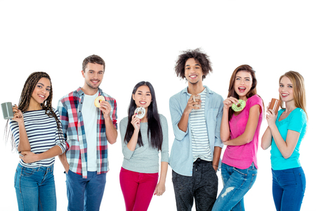 Studio shot of nice young multicultural friends. Beautiful people with cups of coffee and donuts looking at camera and smiling. Isolated backgroundの写真素材