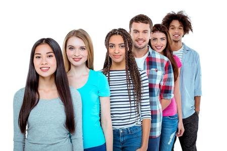 Studio shot of nice young multicultural friends. Beautiful people standing in a row, looking at camera and smiling. Isolated backgroundの写真素材