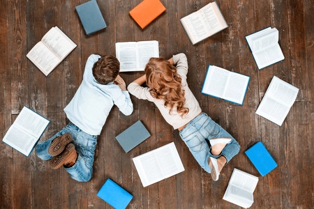 Happy children. Top view creative photo of little boy and girl on vintage brown wooden floor. Children lying near books and reading itの写真素材