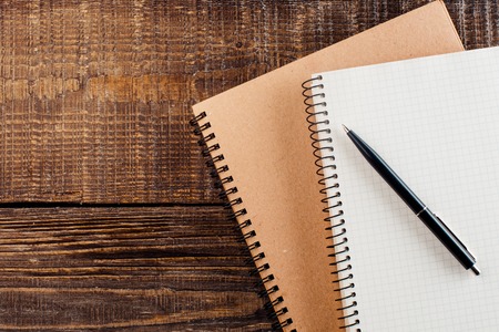Top view photo of objects on wooden table. There are two notebooks with springs and stylish pen.