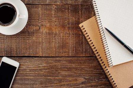 Top view photo of objects on wooden table. There are two notebooks with springs, mobile phone, cup...