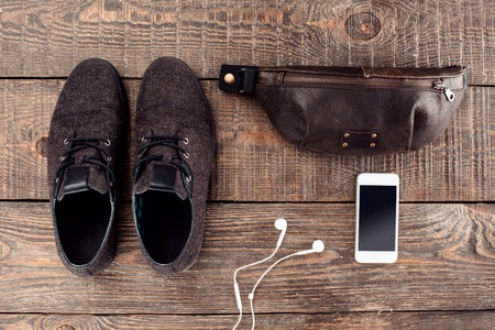 Top view photo of objects on wooden table. There are mobile phone, men's shoes and bagの写真素材