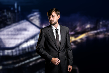 Stylish young businessman on night cityscape background. Businessman looking asideの写真素材