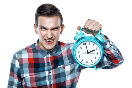 Portrait of stylish handsome young man isolated on white background. Displeased man holding alarm clock and looking at cameraの写真素材