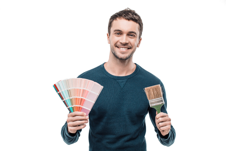 Portrait of stylish handsome young man isolated on white background. Man smiling, looking at camera and holding color palette with brushの写真素材