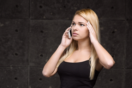 Portrait of stylish beautiful young blonde woman. Woman using mobile phone while having headacheの写真素材