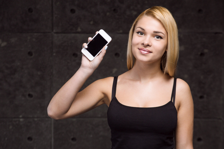 Portrait of stylish beautiful young blonde woman. Woman looking at camera, smiling and holding mobile phoneの写真素材