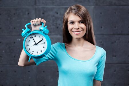 Portrait of stylish beautiful young woman. Woman smiling and holding alarm clockの写真素材