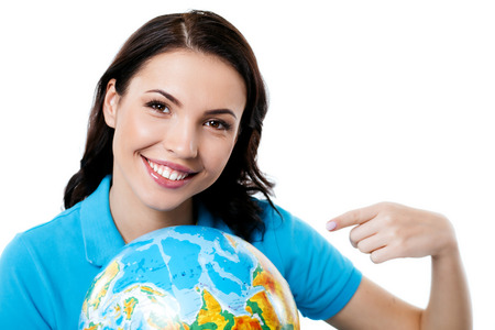 Travel concept. Portrait of stylish beautiful young woman isolated on white background. Woman smiling, looking at camera and pointing at globeの写真素材