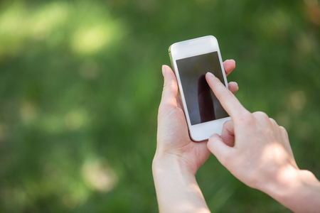 Close up photo of young woman outdoors. Woman holding mobile phone. Beautiful green grass as a backgroundの写真素材