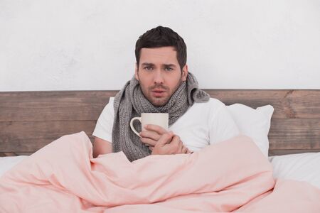 Sick young man drinking hot beverage conceptの写真素材