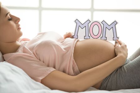 Young preganant woman expecting a baby relaxing on bed indoorsの写真素材