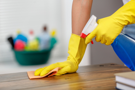 Close up studio shot of housekeeper. Beautiful woman cleaning table with spray. Woman wearing gloves. Focus on handsの写真素材