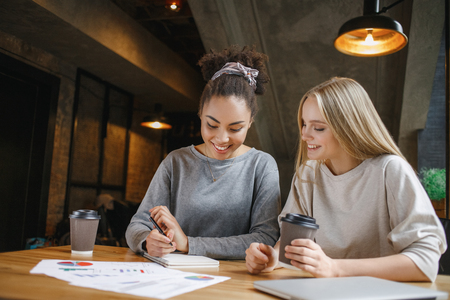 Young women students having a business lunch drinking coffee taking notes creative ideas in planner smiling cheerfulの写真素材