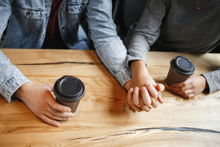 Young boyfriend and girlfriend diverse couple students having a romantic coffee-break drinking hot coffee holding hands closeness concept close-upの写真素材
