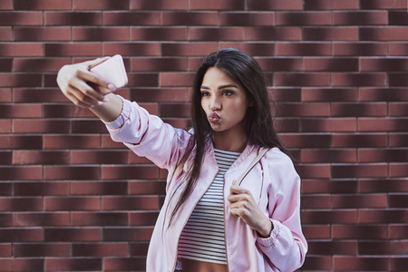 Young woman in pink jacket standing isolated on wall taking selfの写真素材
