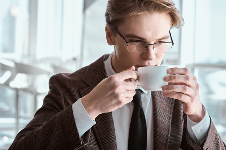 Young businessman in eyeglasses at office sitting drinking coffeの写真素材