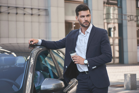 Confident businessman. Handsome young businessman in suit standing near carの写真素材
