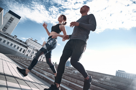 Urban sports. Full length of young couple in sport clothing running through the city street togetherの写真素材