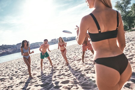 Time with friends. Group of young people playing freesby on the beachの写真素材