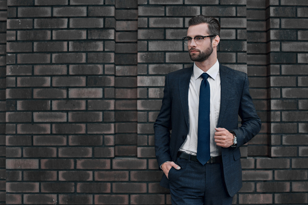 Portrait of a smiling handsome businessman with arms folded over concrete wallの写真素材