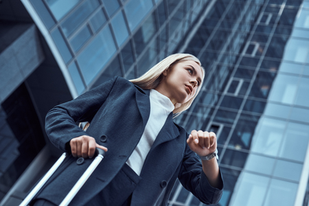 Woman looking at her wrist watch while going to office checking time on the city backgroundの写真素材