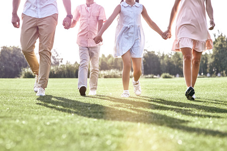 Family walk. Family of four walking on grassy field legs close-uの写真素材
