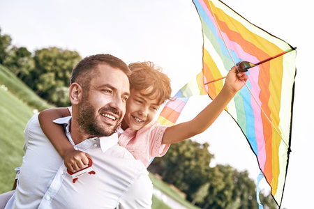 Weekend activities. Father carrying son on his back holding kiteの写真素材