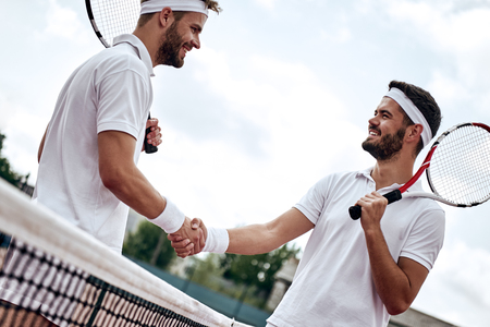 Two men, professional tennis players shake hands before and after the tennis match. One of they has the face of anger. He is trying to intimidate his opponent.の写真素材