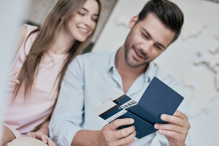 Travel agent and young couple. Young woman smiling and reviwing tickets, passport. Travel agency office interior with big world map in backgrowndの写真素材