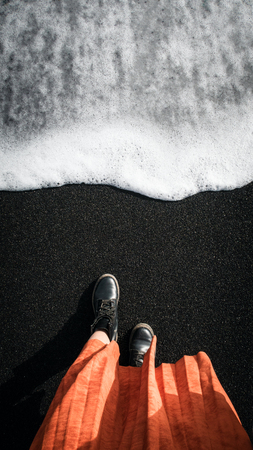 Woman in orange coat at the black volcanic sand. Iclandの写真素材