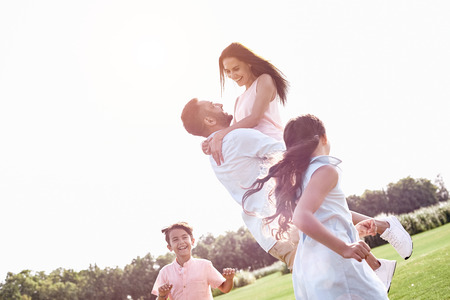 Bonding. Family of four walking on grassy field husband holdingの写真素材