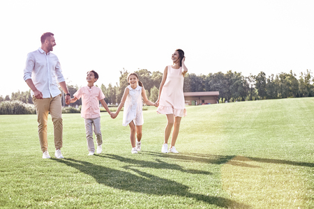 Family walk. Family of four walking on grassy field looking at eの写真素材