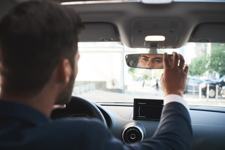 Handsome bisnessman behind the wheel adjusting rear view mirror.