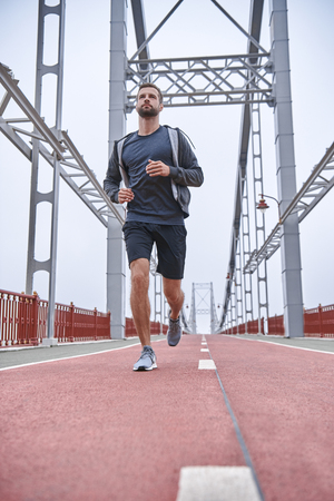 Morning workout. Full length of young man in sports clothing exercising while jogging on the bridge outdoorsの写真素材