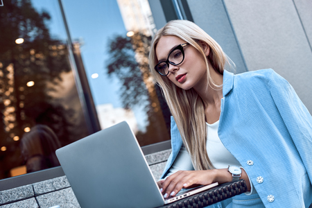 Fashionable businesswoman in glasses sitting in a cafe working with a laptop, her face is focusedの写真素材